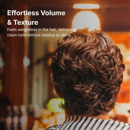 Person with styled hair in a blurred indoor setting, promoting effortless volume and texture.