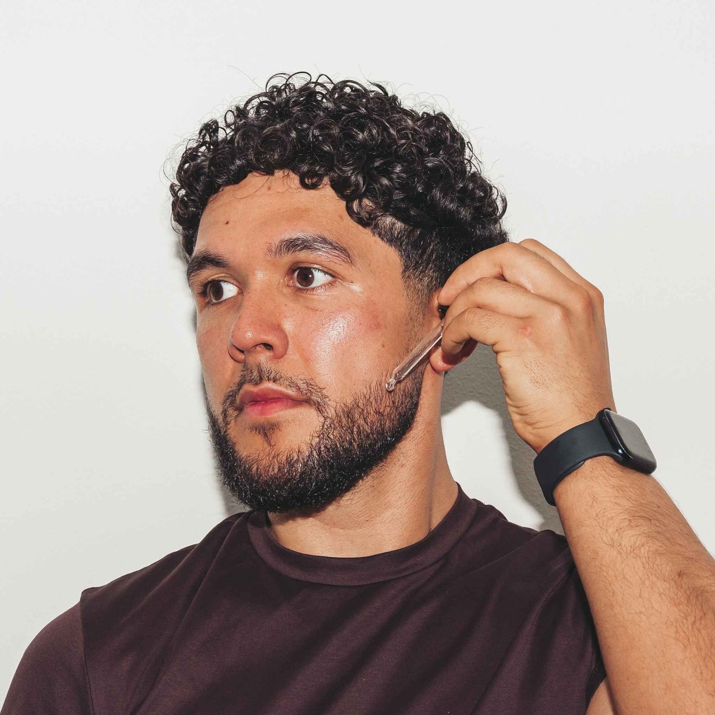 Man with a beard using Beardoil against a plain background