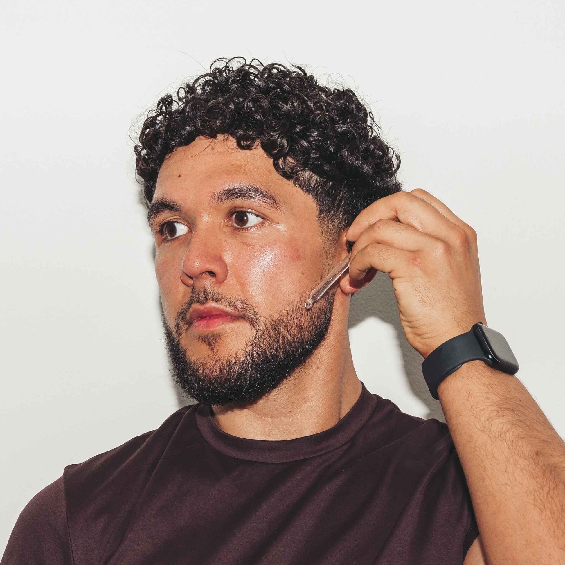 Man with a beard using Beardoil against a plain background