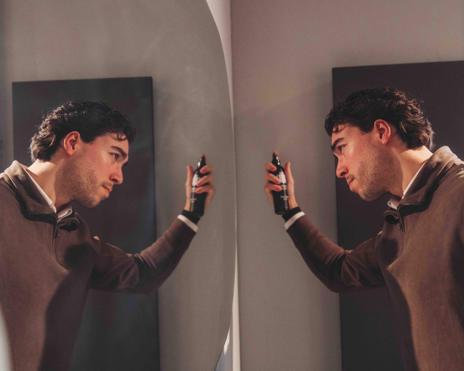 Man holding esseza sea salt spray  to his head in front of a mirror