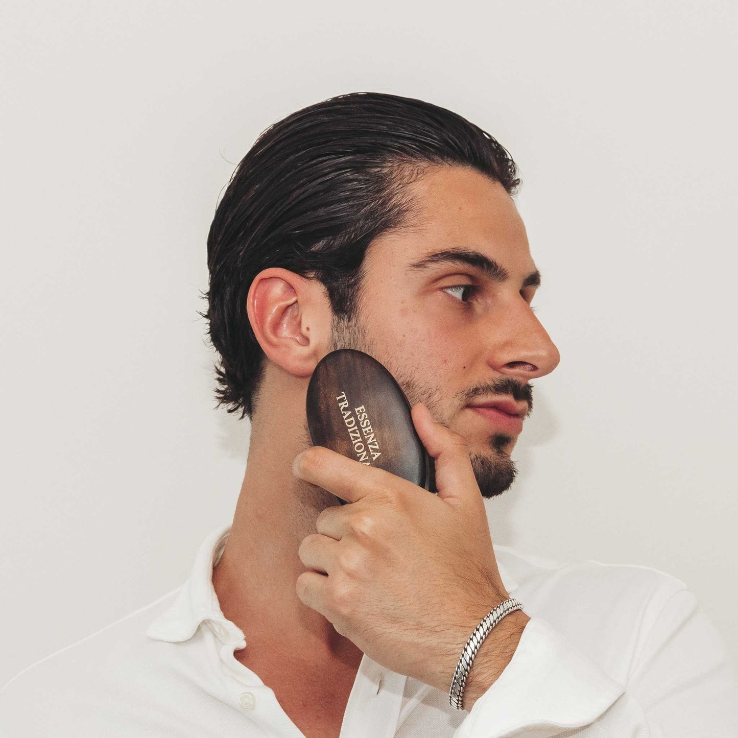 Man using a brown hairbrush with 'Essenza Tradizionela' branding on a white background