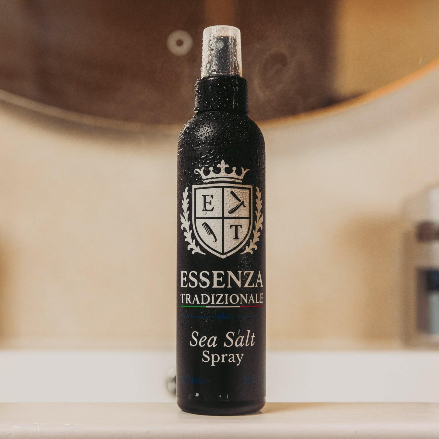 Black spray bottle labeled 'Essenza Tradizionale' with 'Sea Salt Spray' on a blurred background