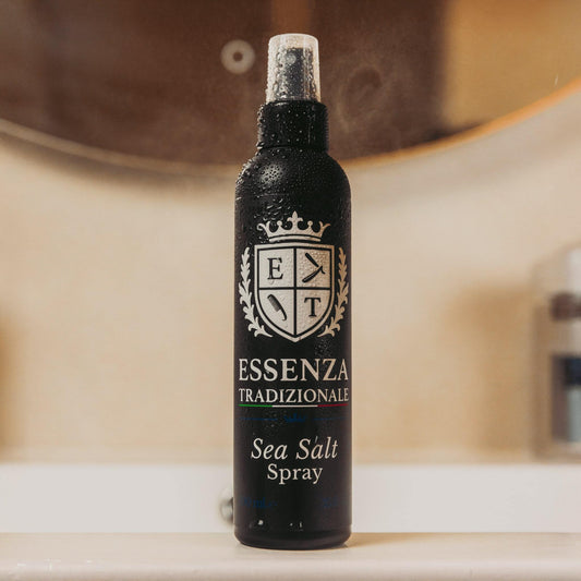 Black spray bottle labeled 'Essenza Tradizionale' with 'Sea Salt Spray' on a blurred background